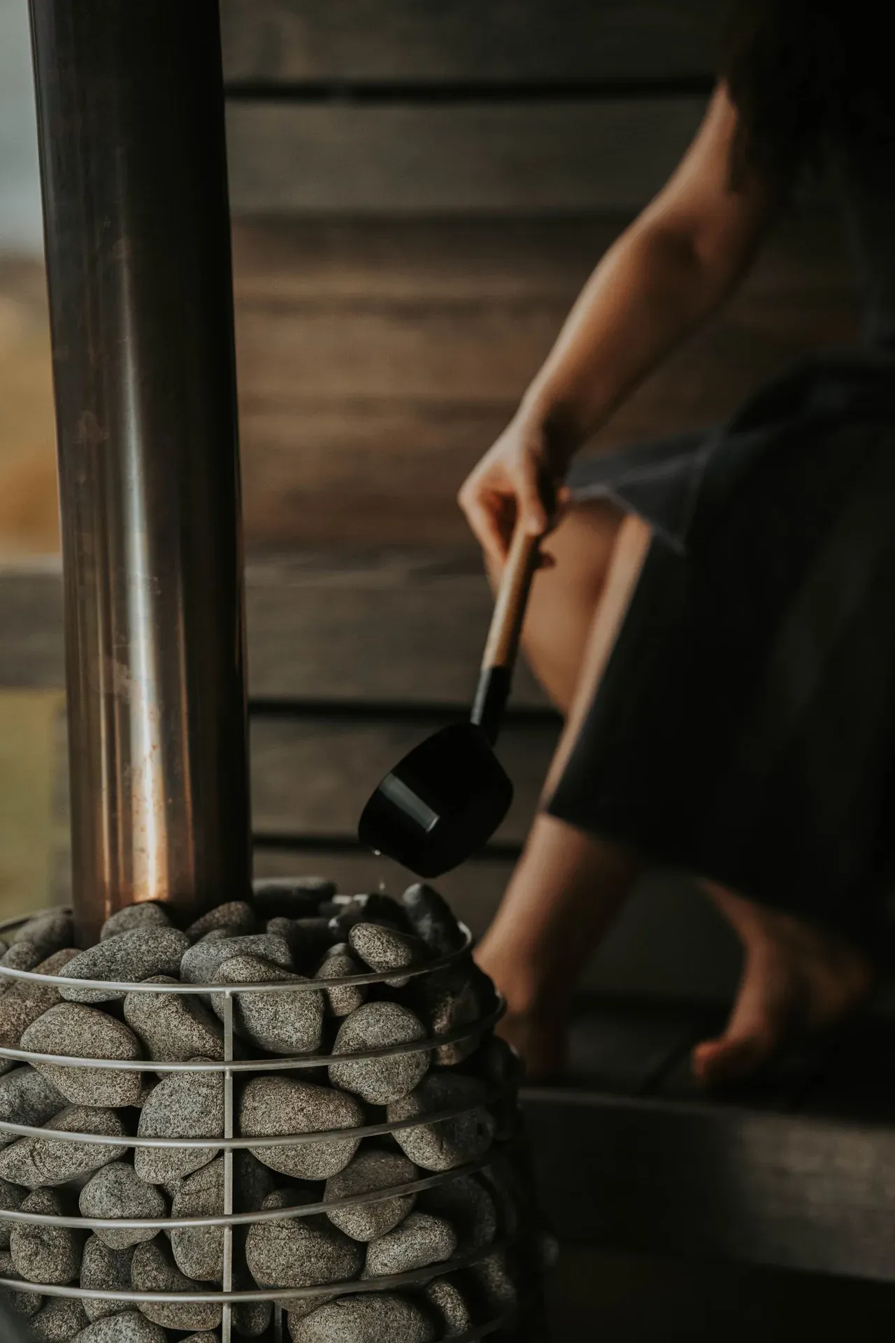 Persona echando agua sobre las piedras calientes de una sauna tradicional para generar vapor (löyly)